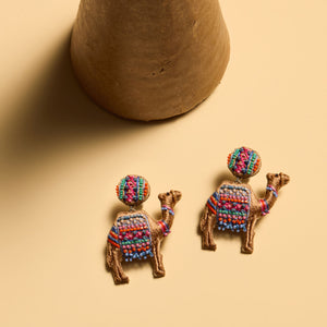 Beaded and Embroidered Camel Earrings Staged on Flat Cream Background with Vase