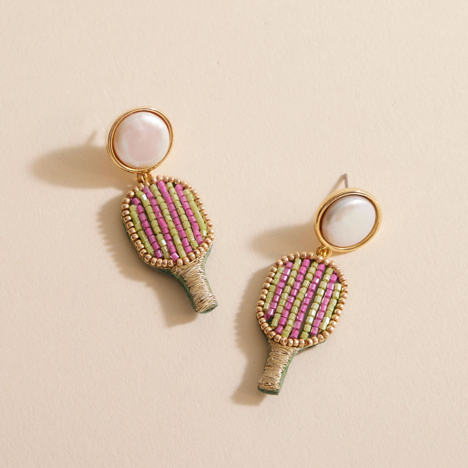Pink and Gold Pickleball Racket Drop Earrings on Tan Background