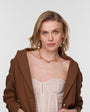 Woman wearing a brown jacket over a sheer top with the Bianca Necklace on a plain background