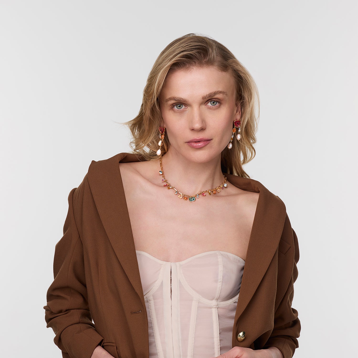 Woman wearing a brown jacket over a sheer top with the Bianca Necklace on a plain background