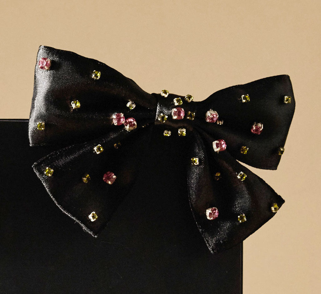 Black bow with embedded colorful crystals on a beige background