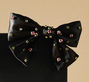 Black bow with embedded colorful crystals on a beige background