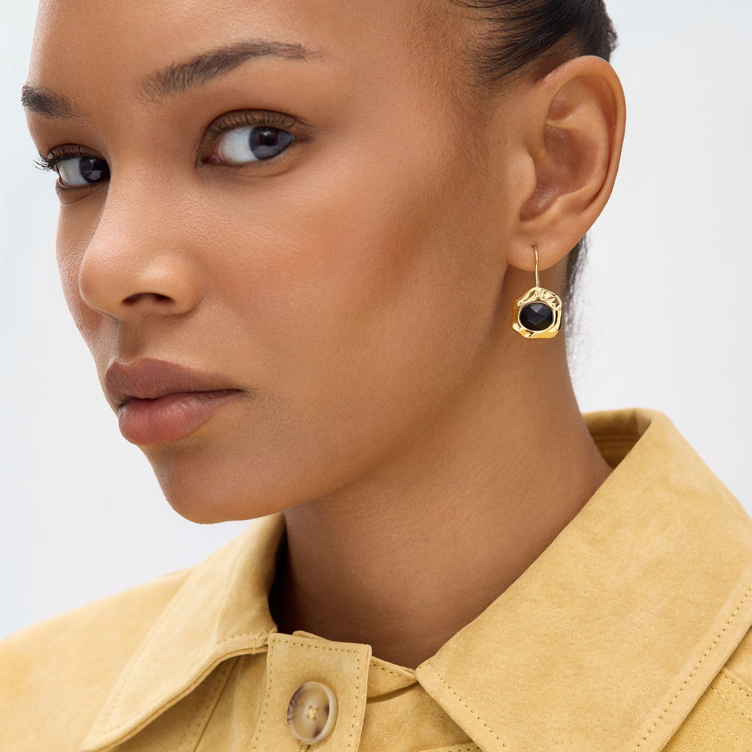 Person wearing yellow top and gold earrings with black crystal center on plain background