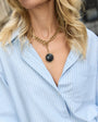 Woman wearing a gold chain necklace with a black pendant, blurred background