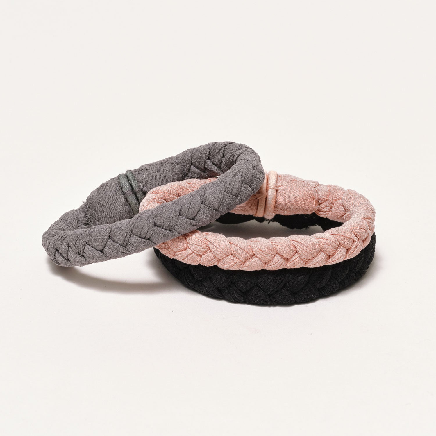 Three Braided Bracelets in Nude, Grey, and Black on Tan Background