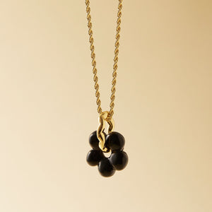 Black Glass Flower Charm on Gold Chain on Flat Cream Background