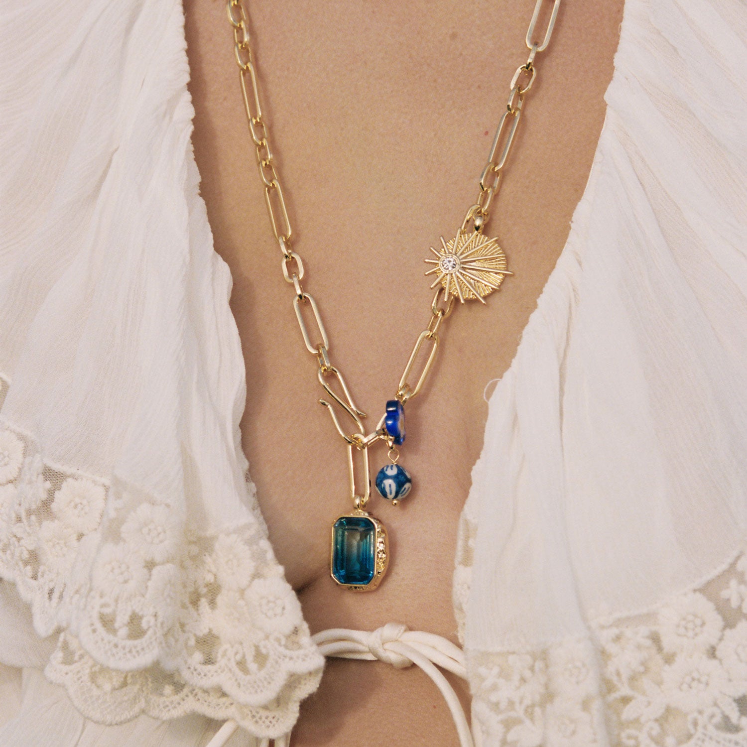 Gold chain necklace with blue pendant on a person wearing a white lace garment.