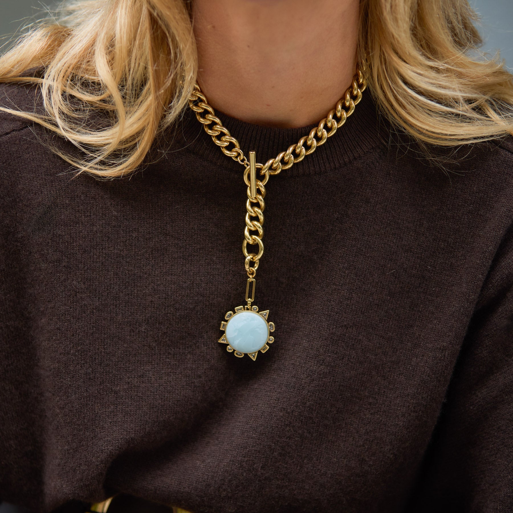 Gold chain necklace with a blue pendant worn by a person against a neutral background