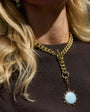 Close-up of a gold chain necklace with a blue pendant worn by a person with blonde hair.