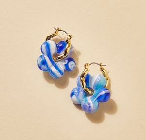Blue and White Marbled Glass Flower Charm Earrings on Gold Hoops on Flat Cream Background