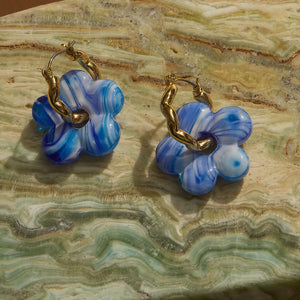 Blue and White Marbled Glass Flower Charm Earrings on Gold Hoops Styled on Marble Background