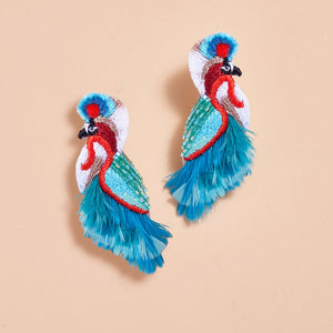 Blue, Red, White, and Black Embroidered and Beaded Feather Bird Earrings on Tan Background