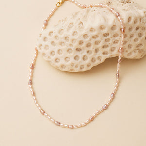 Blush Pearl Strand Necklace Staged on Coral on Flat Cream Surface