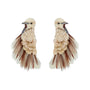 A pair of statement earrings shaped like birds, featuring cream-colored feathers, scalloped beige and gold beadwork, and dark brown feather accents, set against a plain white background.