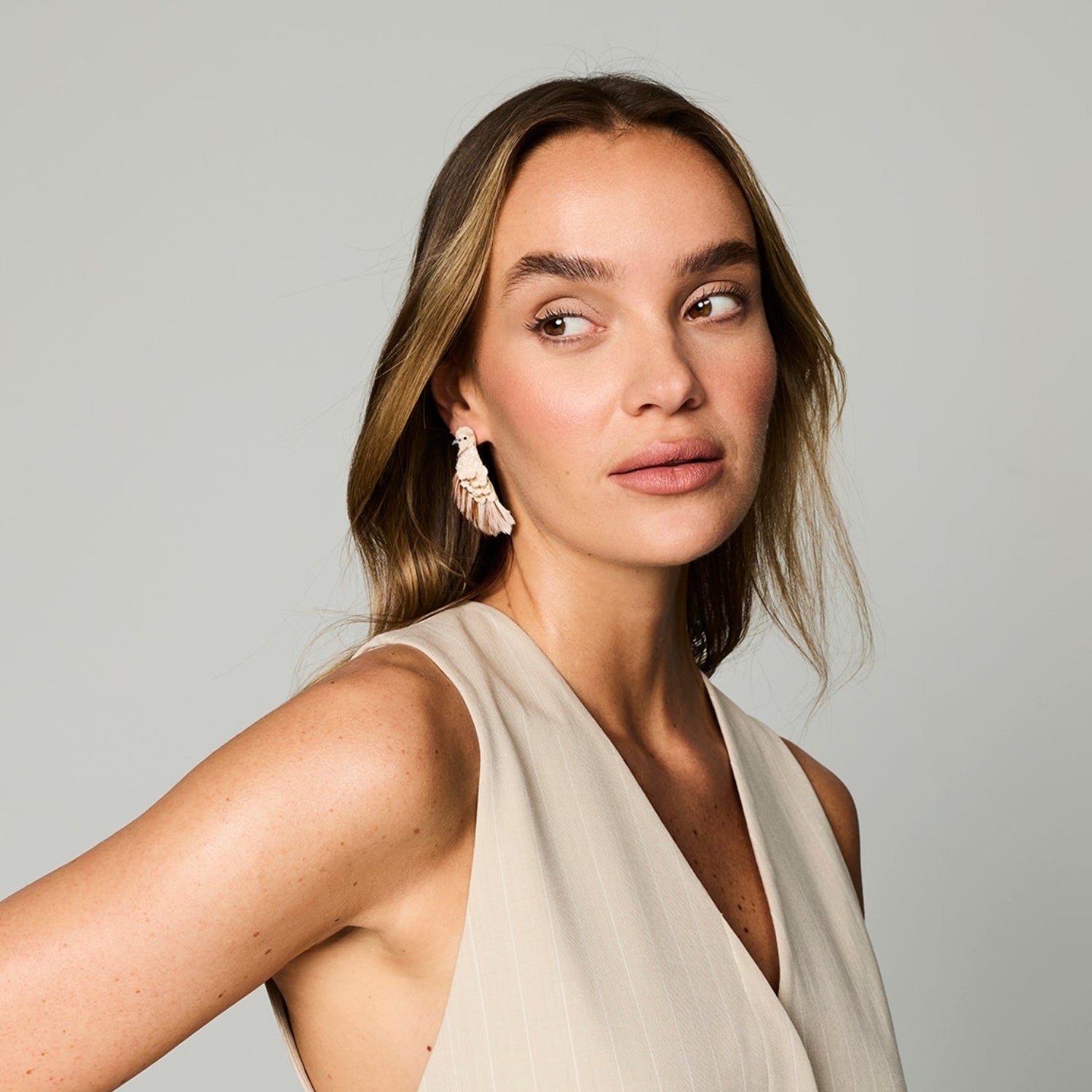 Model wearing bird shaped embroidered earrings with beads and feathers against a white background