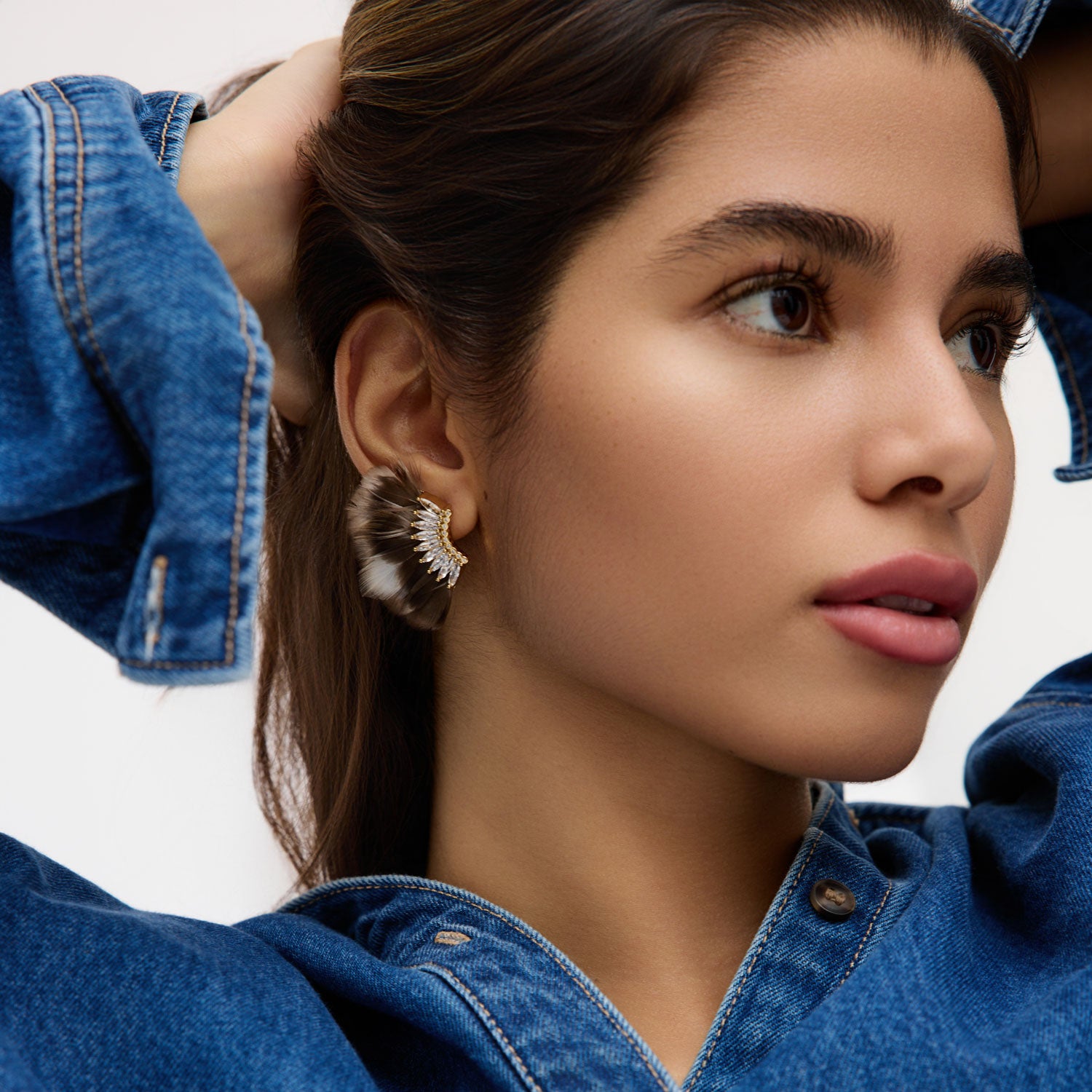 Woman wearing a denim jacket with a close-up of her earring against a neutral background