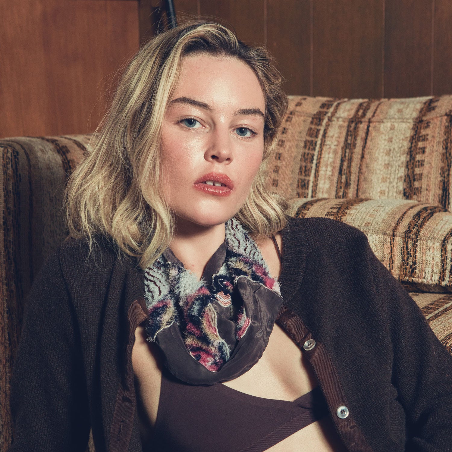Woman wearing a patterned scarf sitting on a textured couch.