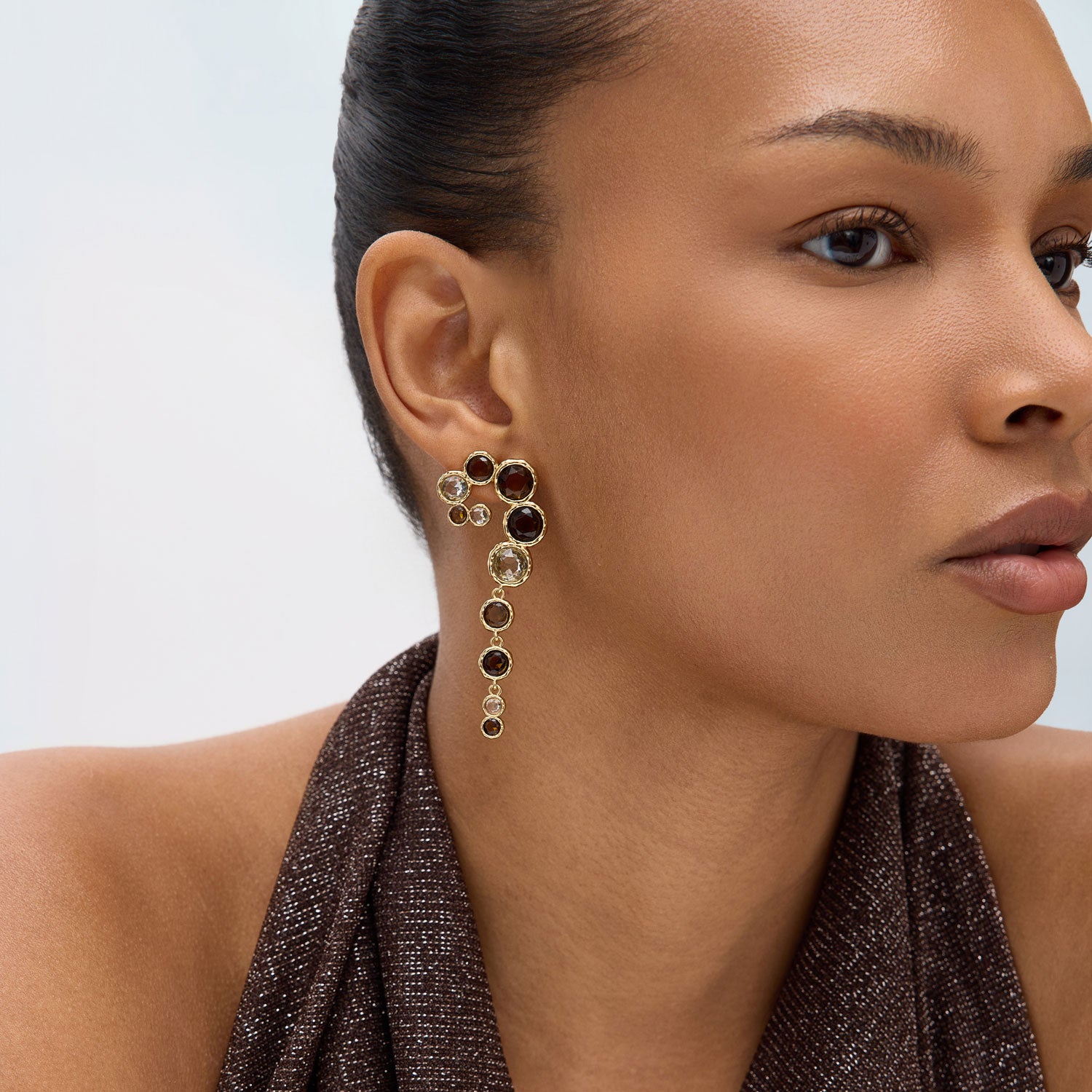Close-up of a woman wearing a set of dangling earrings with a neutral background
