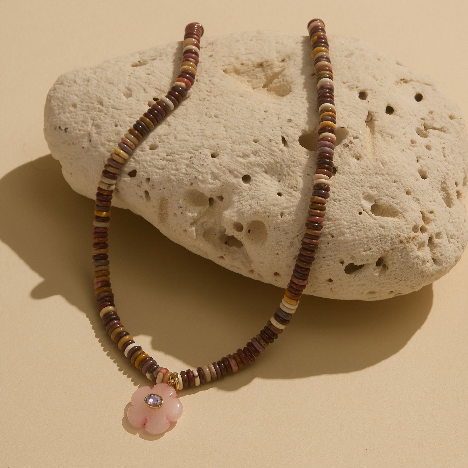 Brown Beaded Strand Necklace with Pink Flower Charm on Cream Coral Staged on Flat Cream Background