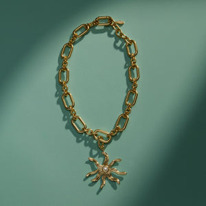 Gold Chain Necklace with Gold and Crystal Star Sun Charm on Green Surface