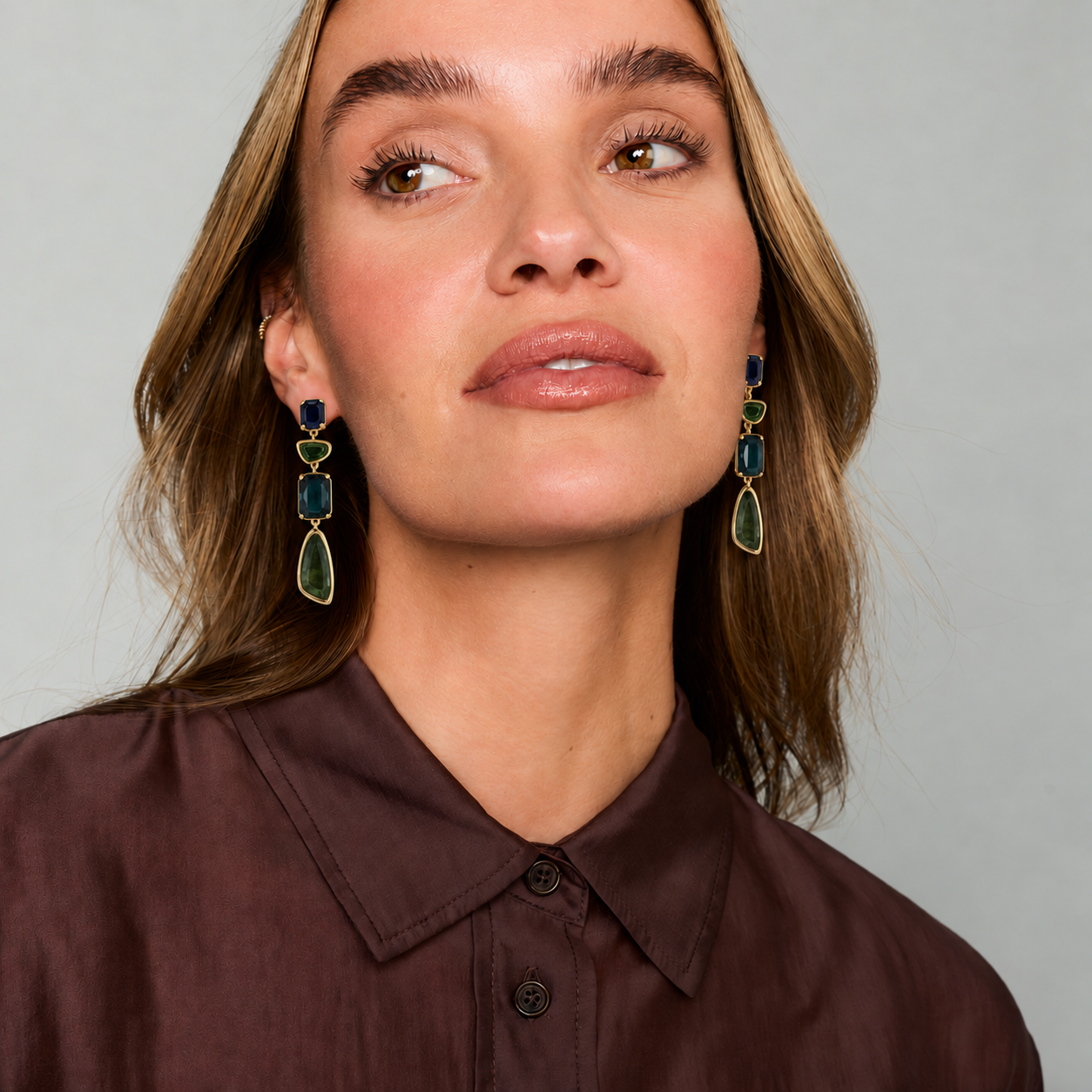 Gold-tone drop earrings featuring blue, teal, and clear faceted stones in a layered geometric design on white