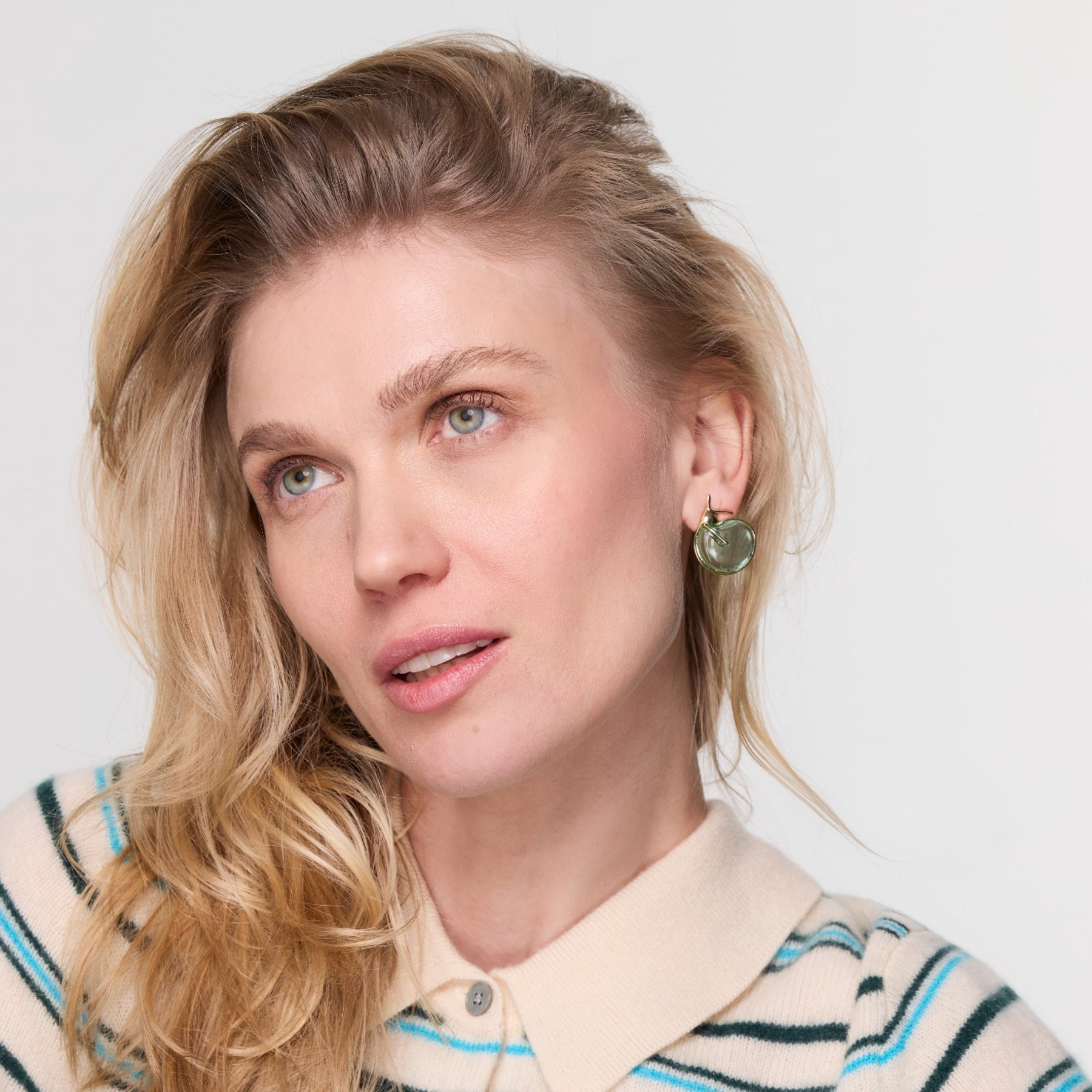 Blonde model wearing striped shirt and glass green earring studs. 