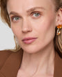 Close-up of a woman wearing gold earrings with a orange drop stone against a light background