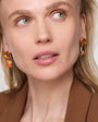 Close-up of a woman wearing gold earrings with orange gemstones on a neutral background
