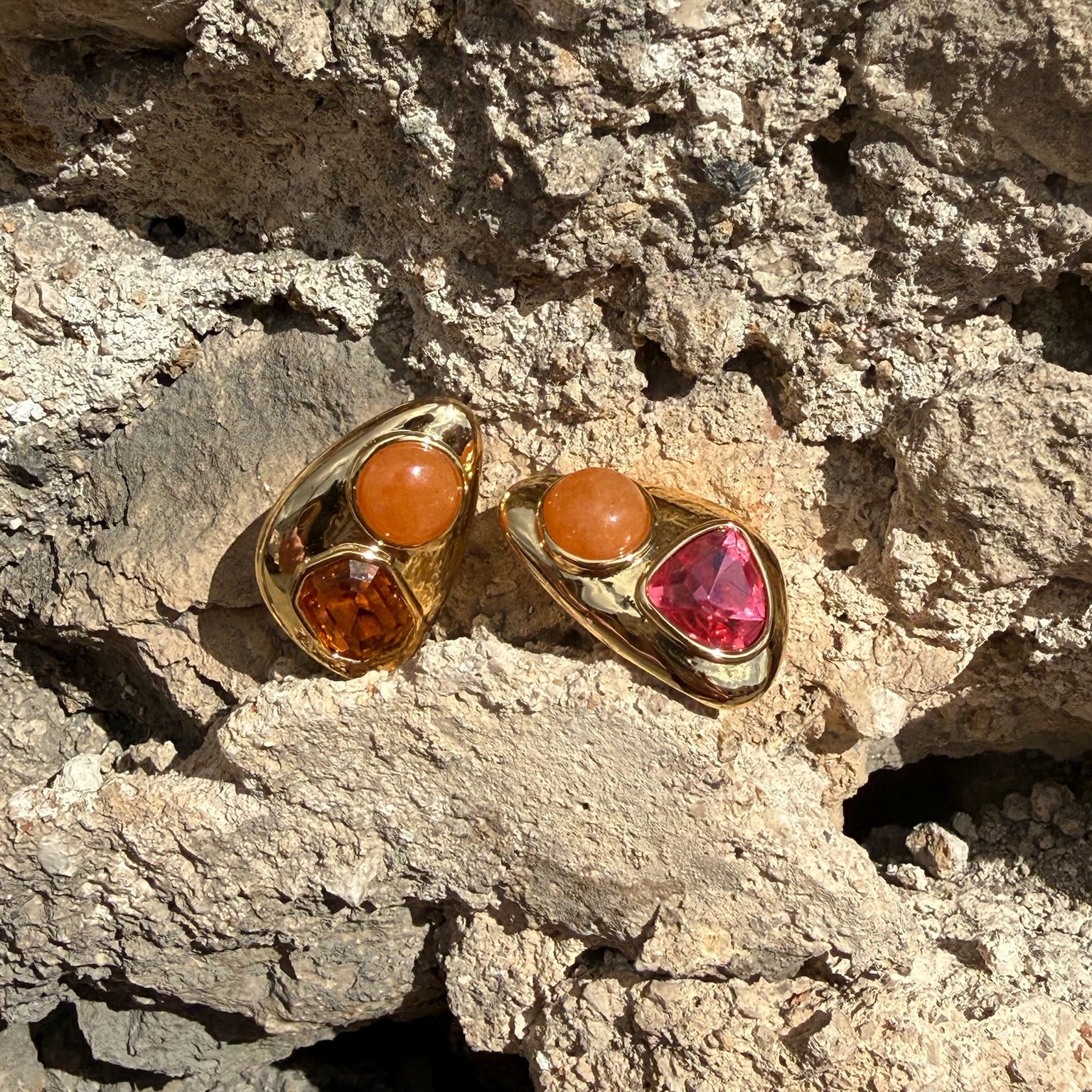 Gold earrings with gemstones on a textured stone surface