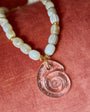 Necklace with shell beads and a pink shell pendant on a red fabric background