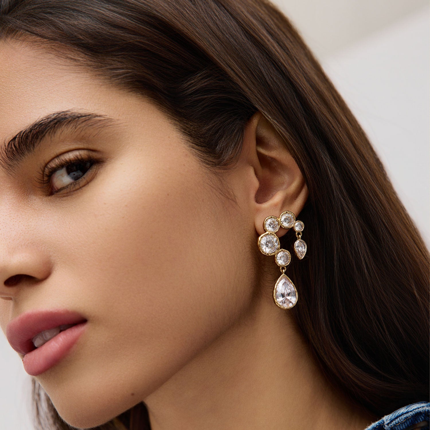 Woman wearing crystal and gold drop earrings on white background