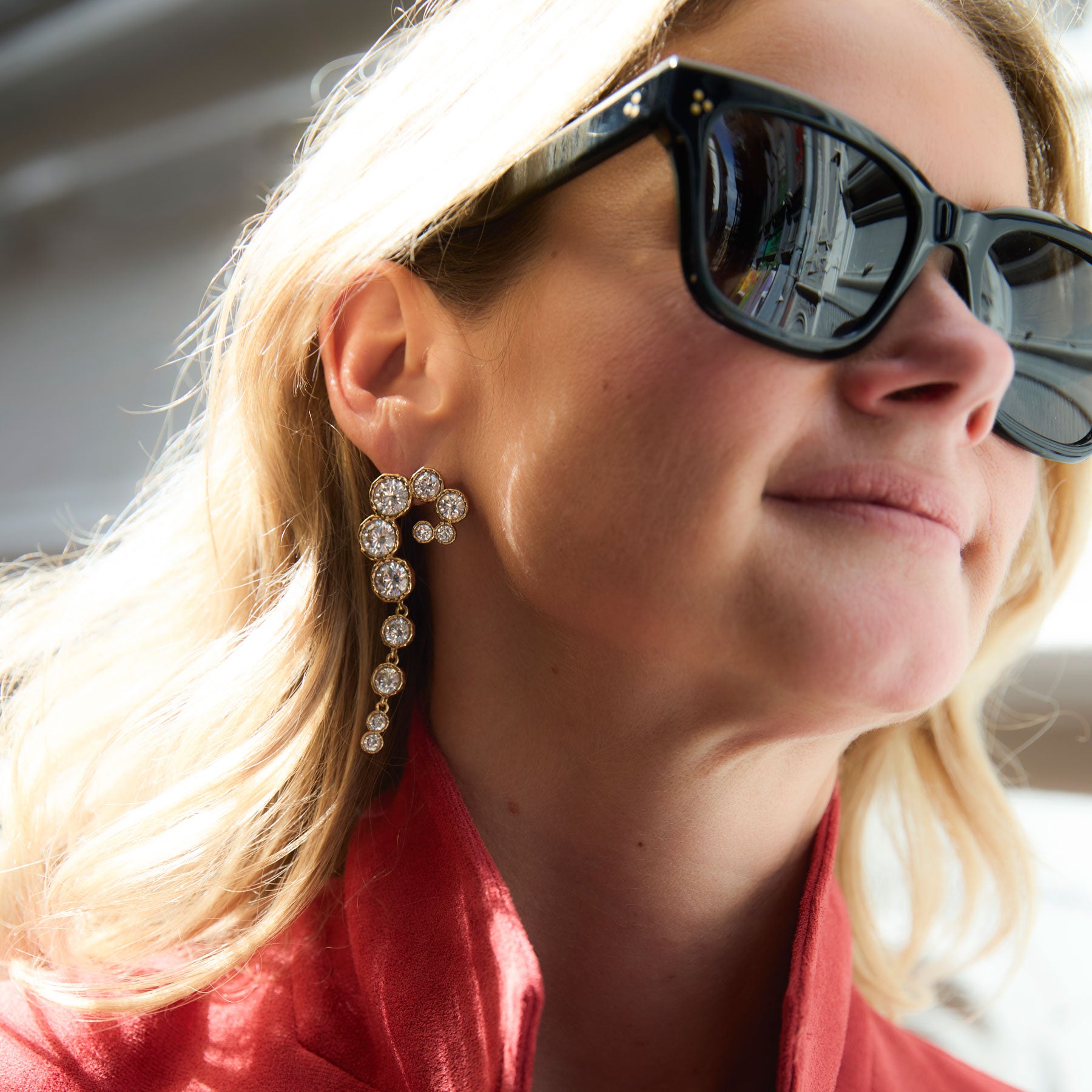 Close up of Maggie wearing crystal statement earrings and black sunglasses 