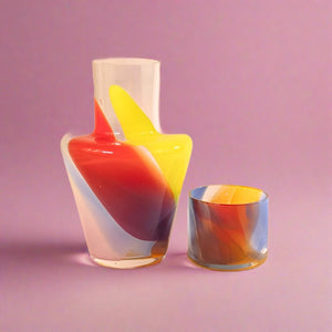 Orange, Yellow, Purple, Red, Pink, and Blue Glass Decanter and Glass on Pink Background