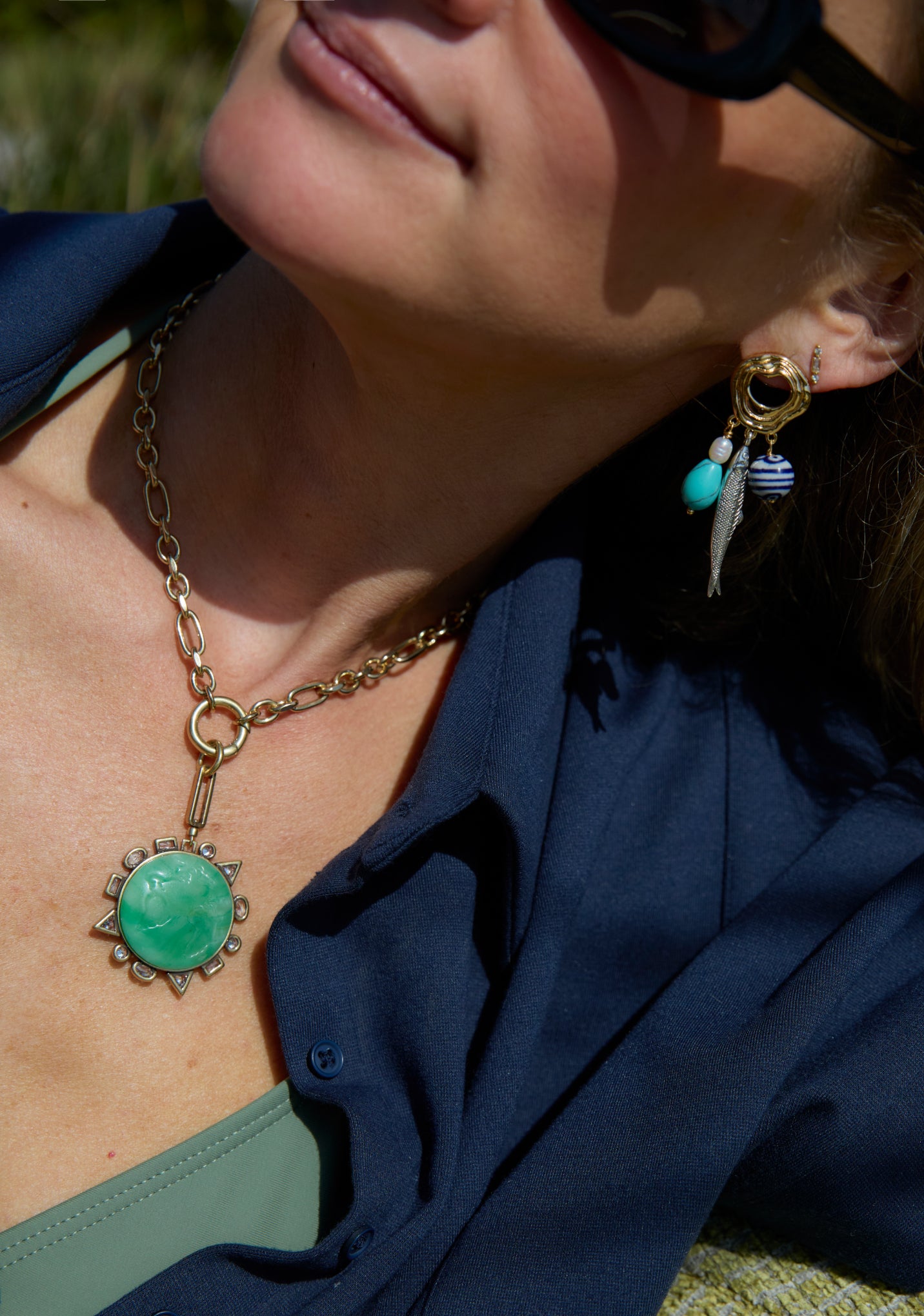 A close-up lifestyle shot of a woman wearing a gold chain necklace with a round green pendant and matching drop earrings.