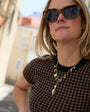 A woman wearing a white top, and a gold-toned link necklace with a pearl and amber pendant, paired with tigers eye heart shaped earrings