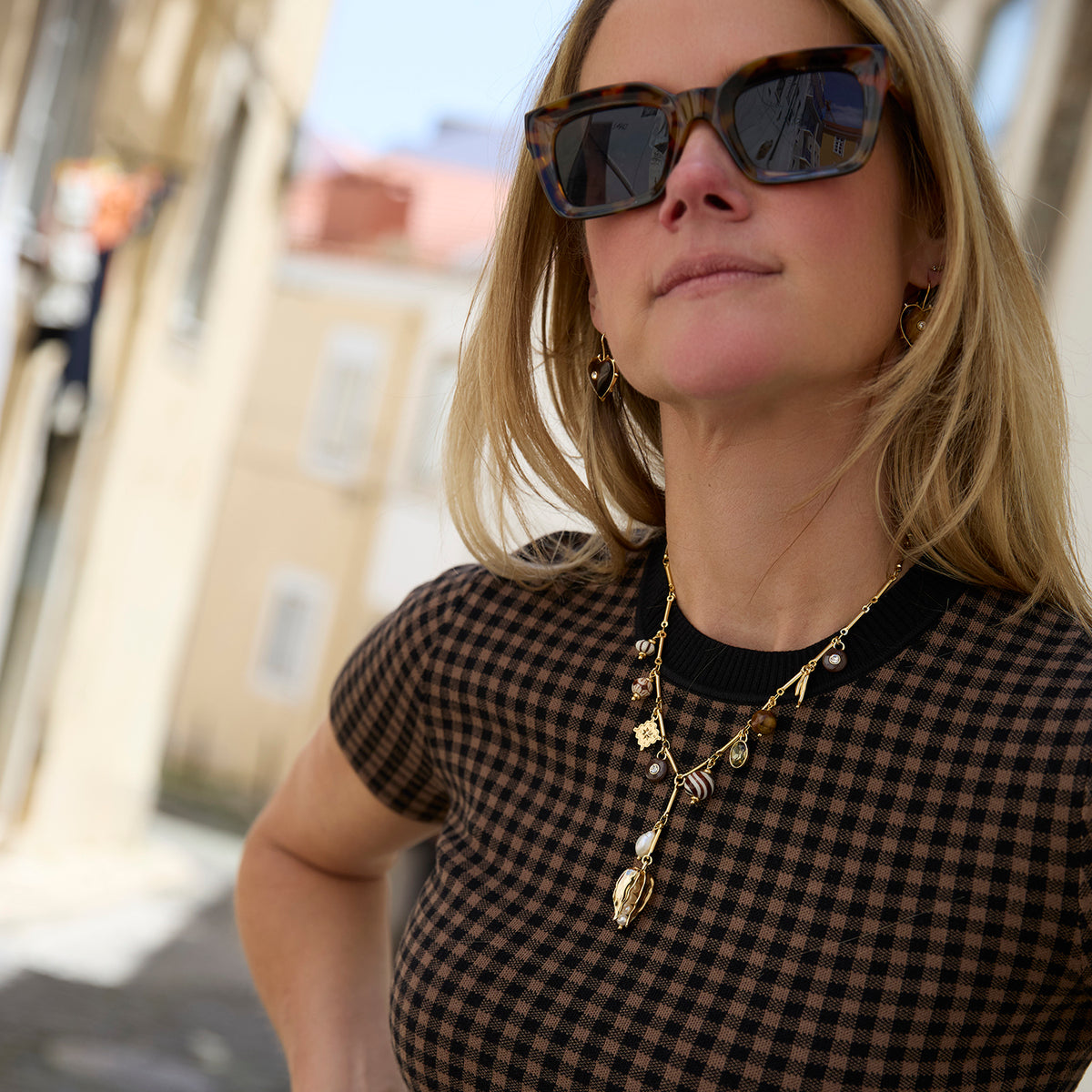 A woman wearing a white top, and a gold-toned link necklace with a pearl and amber pendant, paired with tigers eye heart shaped earrings