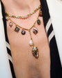 A woman wearing a white top, and a gold-toned link necklace with a pearl and amber pendant, paired with a green and amber colored tennis necklace