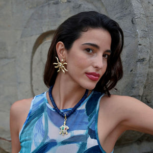 Beaded Strand Necklace with Turtle Charm and Gold Sun Star Earrings on Model in Blue Patterned Dress
