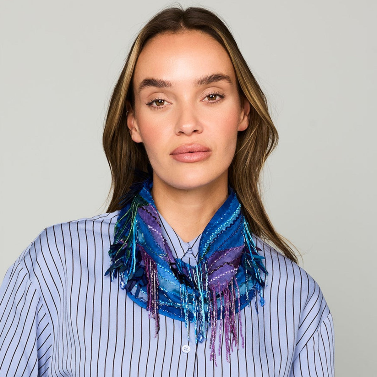 Blue patterned, beaded and embroidered scarf necklace featuring colorful pink and purple details on model straight on 