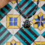 Black beaded necklace featuring a gold-tone Semi Precious Black Onyx pendant with green, navy, blue and clear accents on tile background