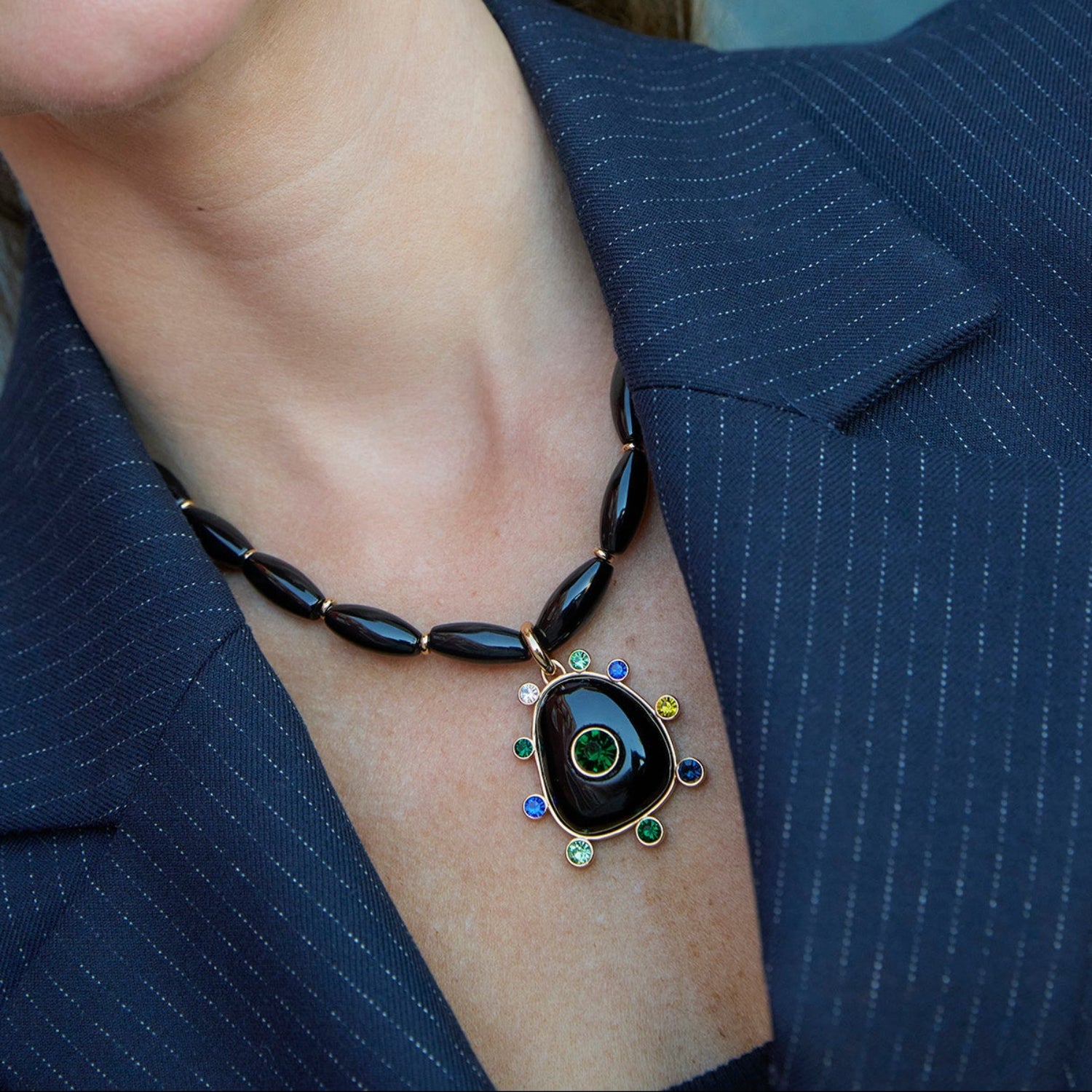 Black beaded necklace featuring a gold-tone Semi Precious Black Onyx pendant with green, navy, blue and clear accents on model close up