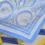 A close-up of a light blue fabric bandana or napkin featuring white block-printed paisley and leaf patterns, laid diagonally over a tiled surface.