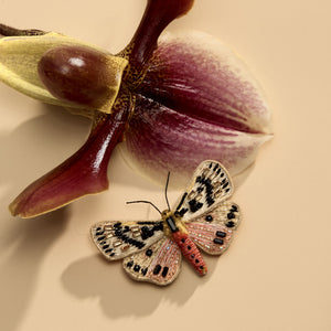 Beaded and Embroidered Butterfly Brooch Staged Next to Orchid Flower on Flat Cream Background
