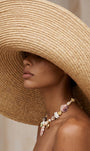 Model wearing large raffia sun hat covering face with large shell charm necklace around her neck