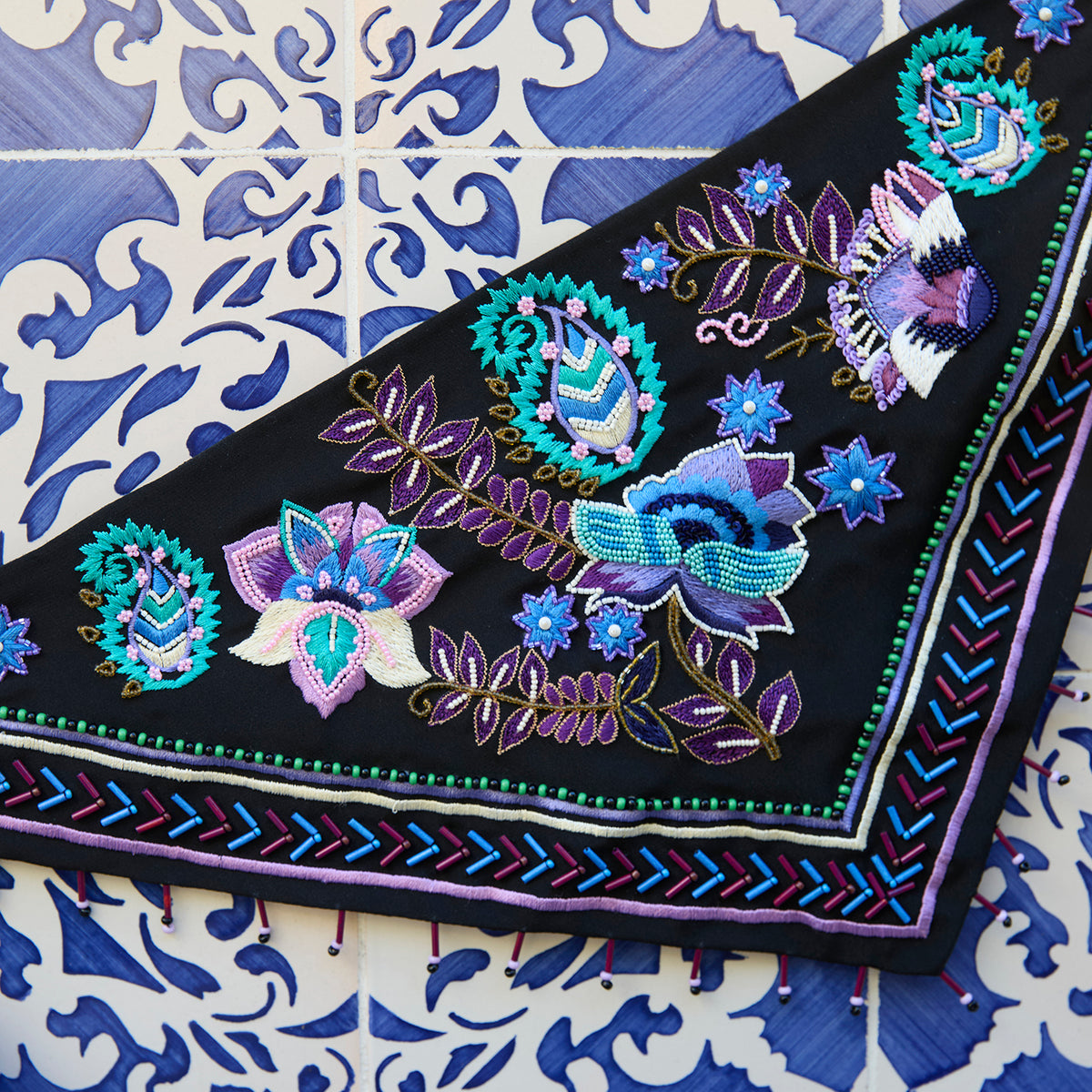 Black scarf necklace featuring colorful floral and geometric embroidery with beaded details on blue and white tile