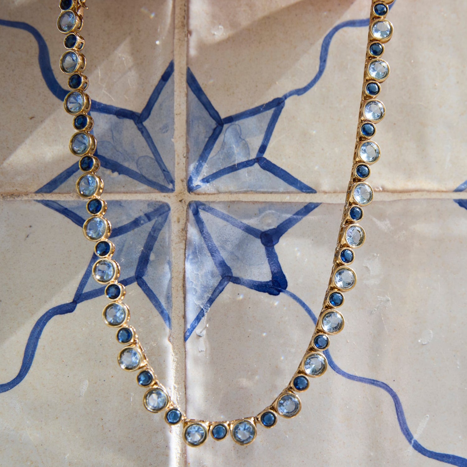 Delicate necklace featuring a strand of small blue beads and a gold-tone clasp with a tile background 