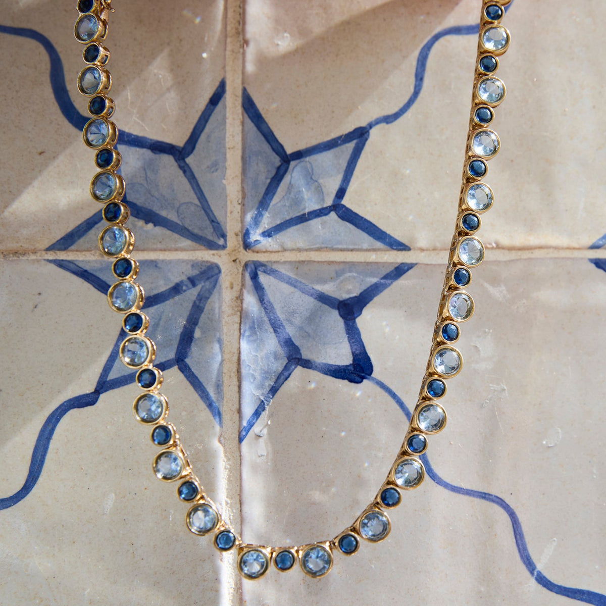 Delicate necklace featuring a strand of small blue beads and a gold-tone clasp with a tile background 