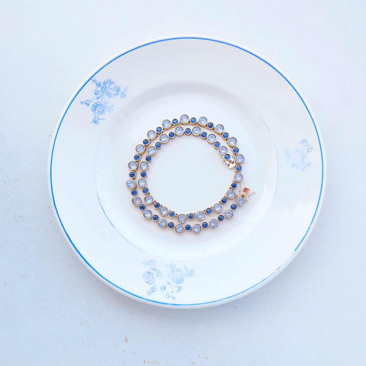 Delicate necklace featuring a strand of small blue beads and a gold-tone clasp styled on a plate