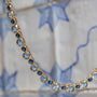 Delicate necklace featuring a strand of small blue beads and a gold-tone clasp with a tile background closeup 