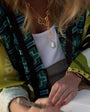 Person wearing a colorful patterned garment with a gold necklace and white sleeve.